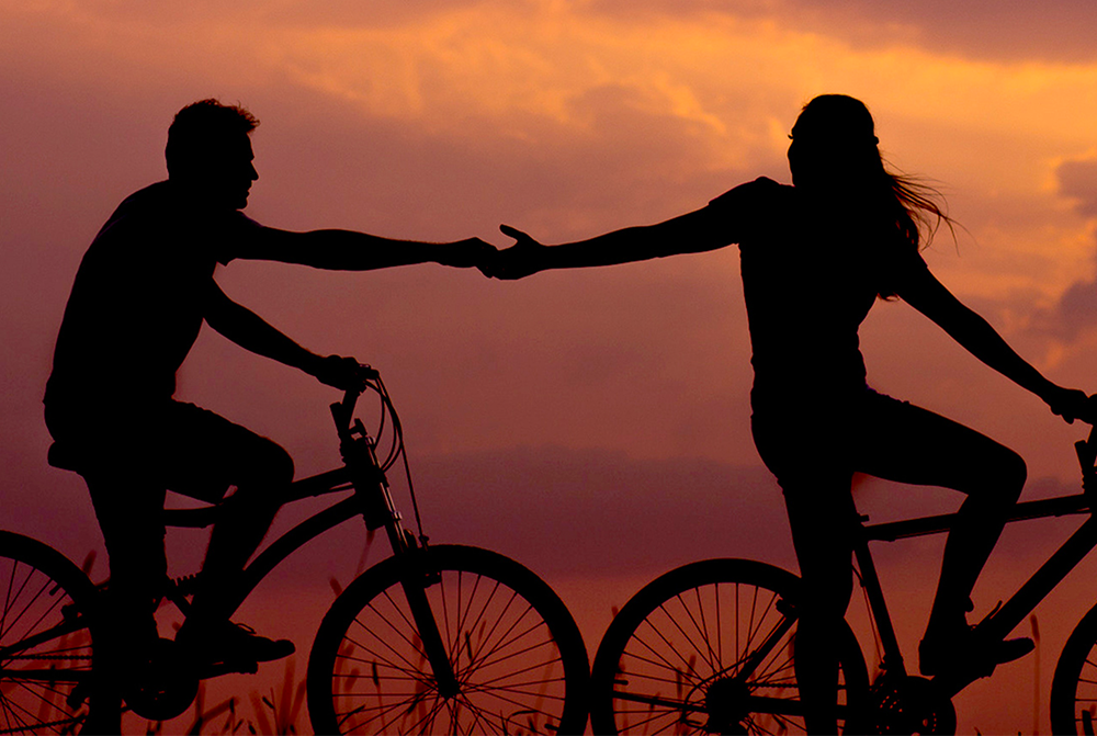 A man and a woman on bicycles reach out to each other and touch hands.