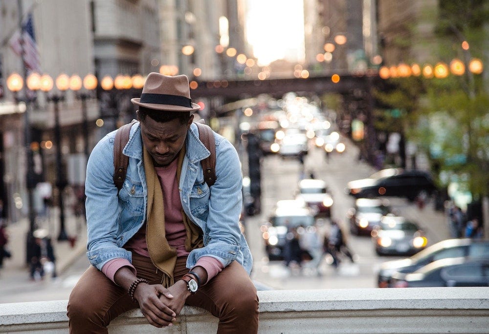 A man sits on a city street with his head looking down.