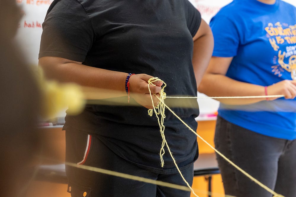 People stand in a circle clutching yellow string from a roll of yarn for a team-building exercise.