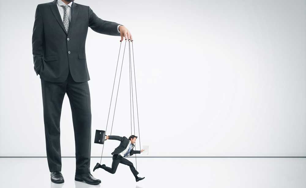 Man in business suit holds strings of male marionette