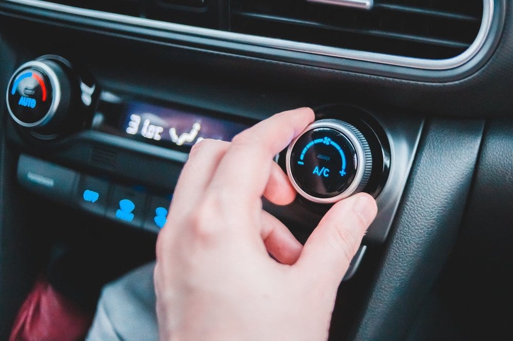 A hand turns an air conditioning knob inside of a car. Modern vehicle interiors have multiple different plastics, textures, and finishes.