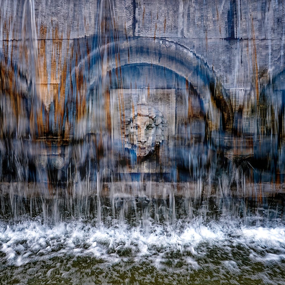 Color image of a lion’s face carved in stone behind a broad water fountain in Tbilisi’s Rustaveli Square