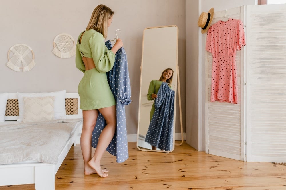 Woman in a green dress standing in front of mirror holding a blue dress.