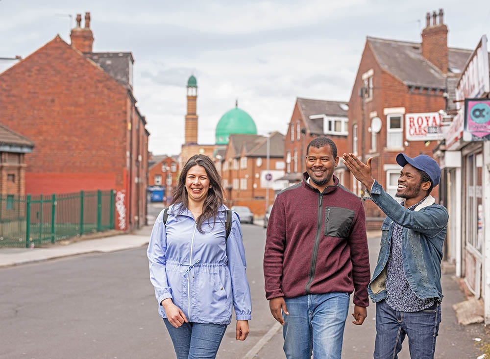 Three students walking through Hyde Park, with a view of a mosque behind them.