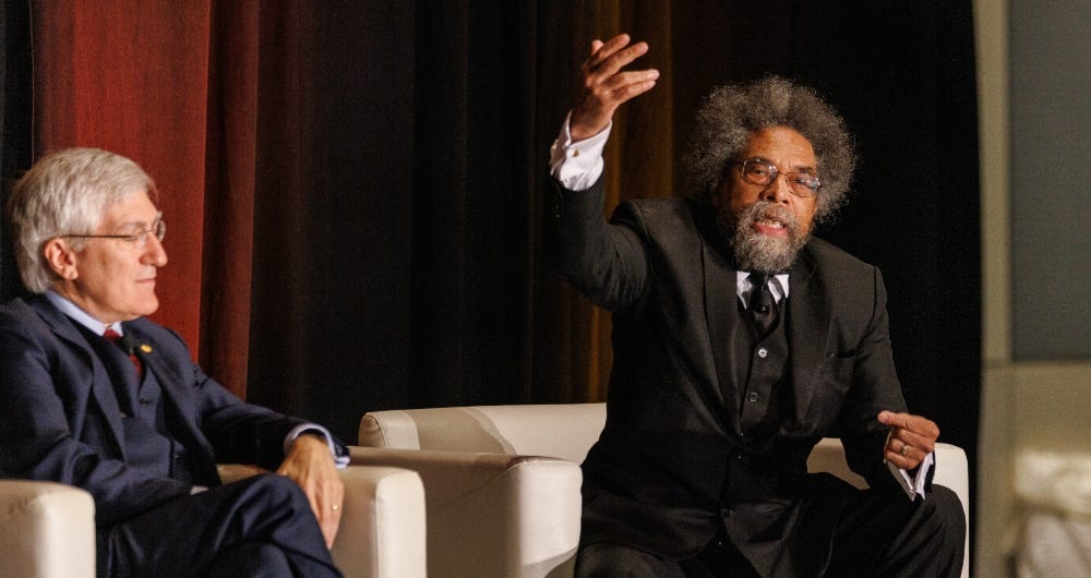Dr. Cornel West and Dr. Robert George engage in conversation, seated on stage
