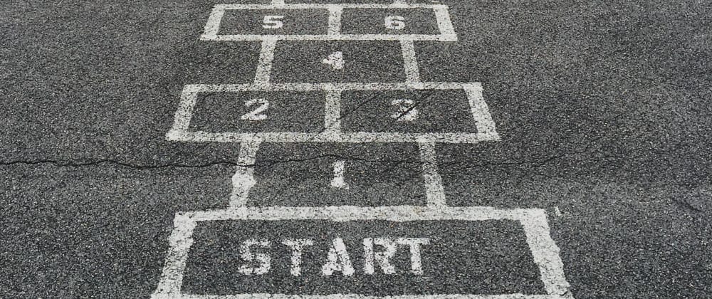 ChatGPT A hopscotch game painted on asphalt, displaying numbers 1 to 6 with “START” at the bottom. The lines are white and slightly worn, indicating the game has been well-used, and the surface shows cracks, suggesting an older playground or schoolyard.
