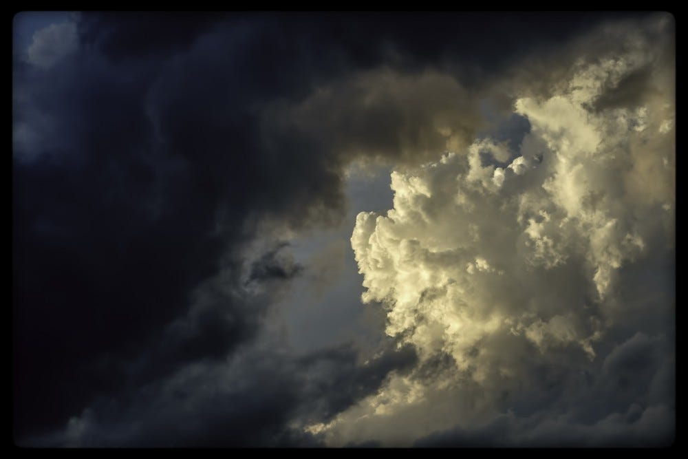 Sky and cloud view, split in half diagonally: black and stormy on left, sunlit and bright on the right.
