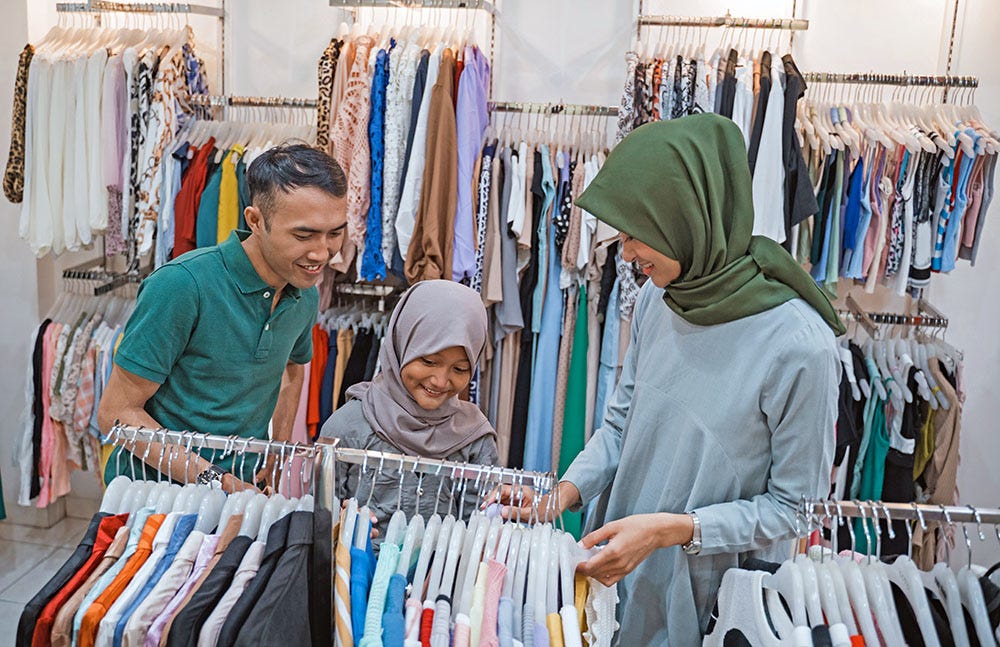 A young couple with a child looking at a selection of clothes in a shop.