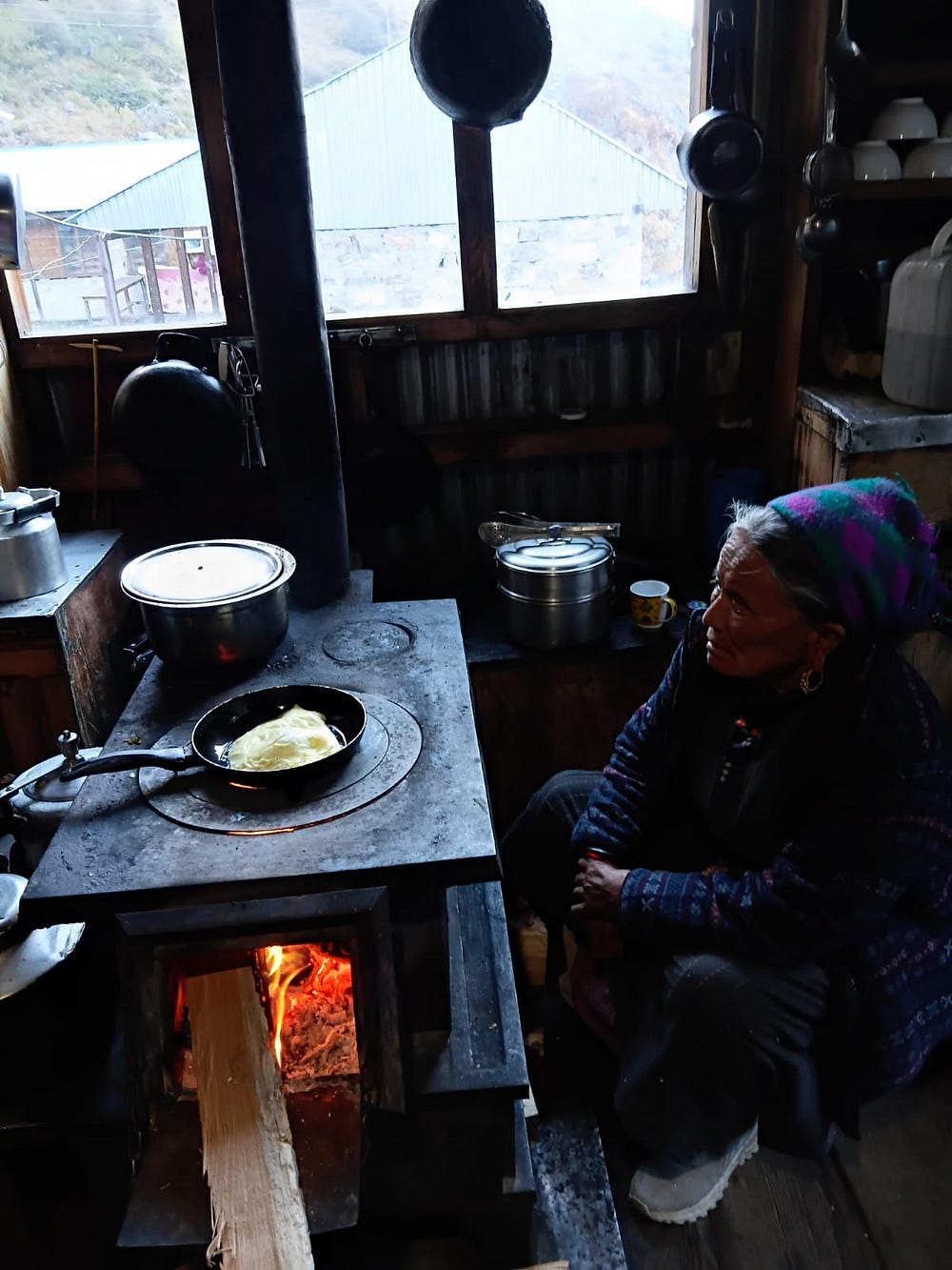 A travel story of Grandma who is sitting in front of the Kitchen in the remote region of Langtang, wearing traditional Tibetan attire as seen in teahouse during Langtang Valley Trek. 