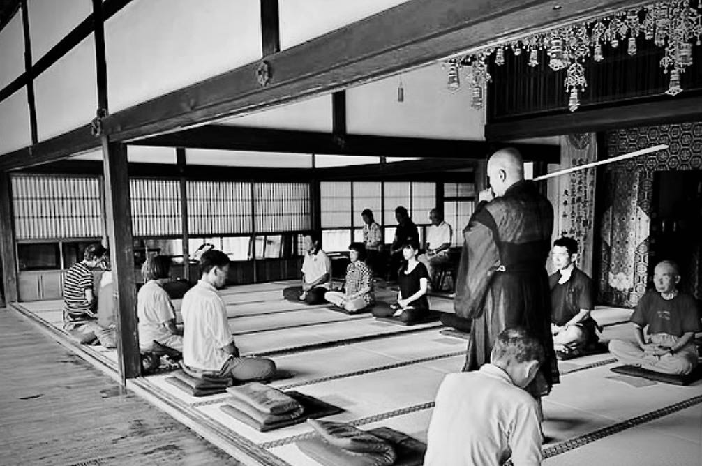 Zazen meditation session in a Kyoto Buddhist temple. A monk is pacing around in front of seated practitioners to assist.