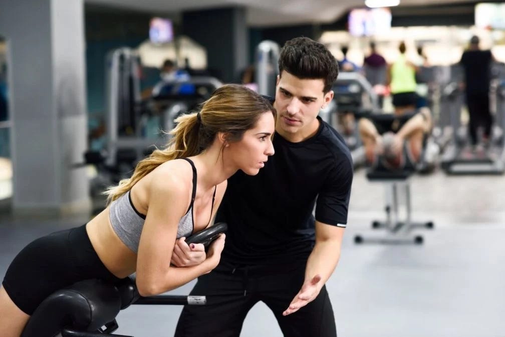 A girl receiving personalized fitness training from a professional trainer in a gym, focusing on proper form and technique.