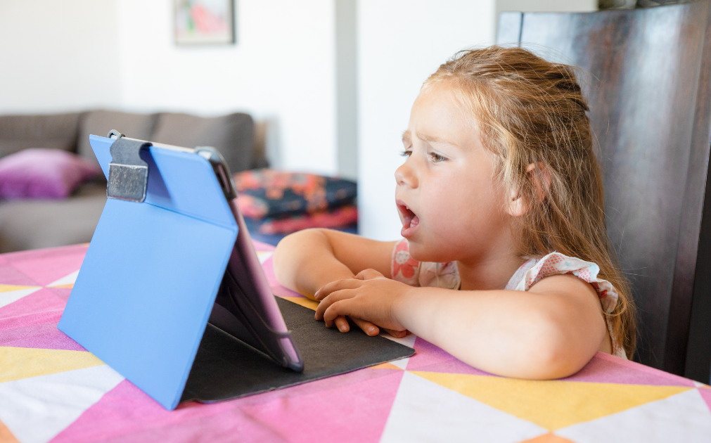 A young girl sitting at a counter, talking into an iPad.