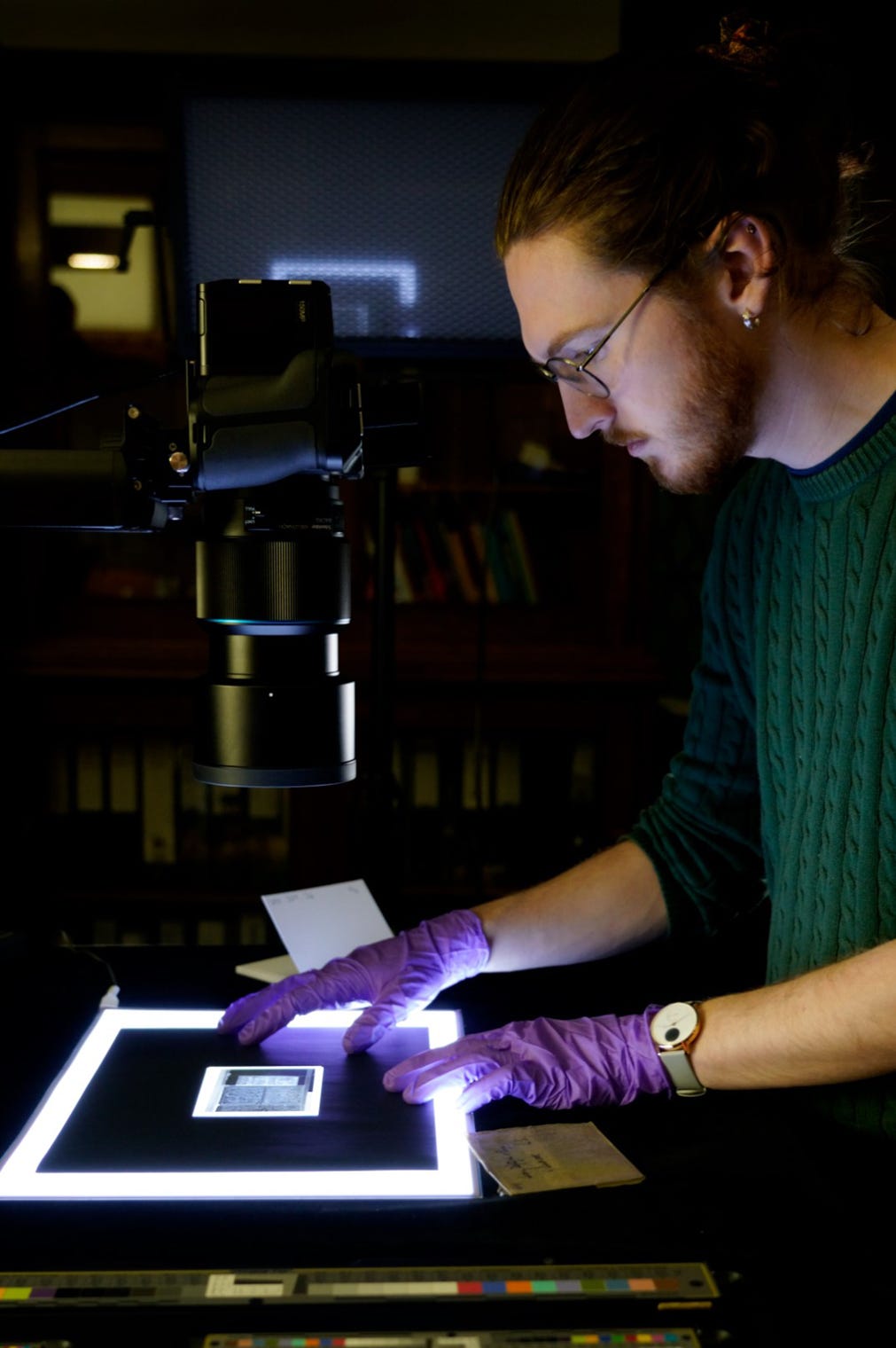 Alex, wearing a green jumper and purple gloves, photographing a quarter-plate glass negative placed on a light sheet