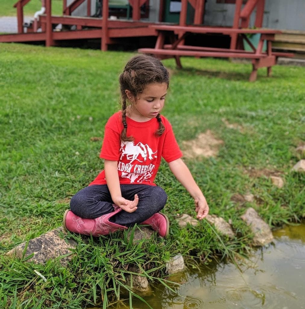 4 year old Lucia pretends to fish at a small pond using a blade of grass