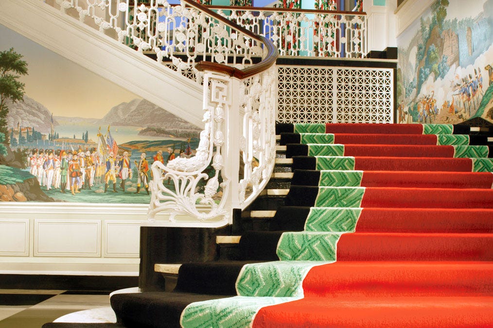 Red carpet on stairwell, white handrails, classical painting and checkerboard floor.