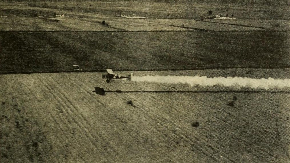 A plane flying over a field as dust trails behind.