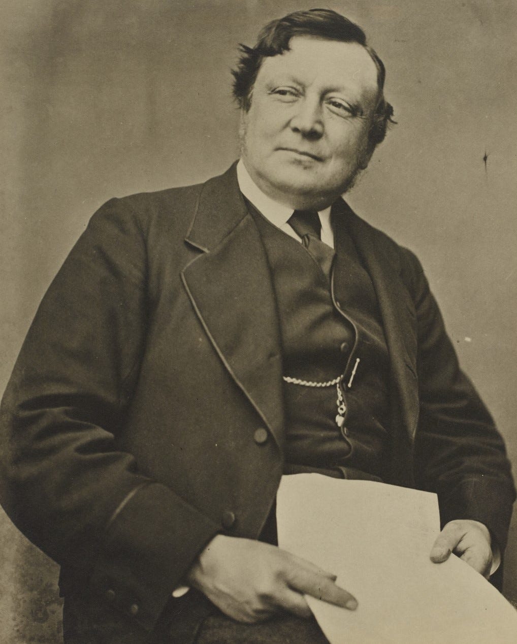 Sepia portrait photograph of Henry Roscoe, seated holding a piece of paper.