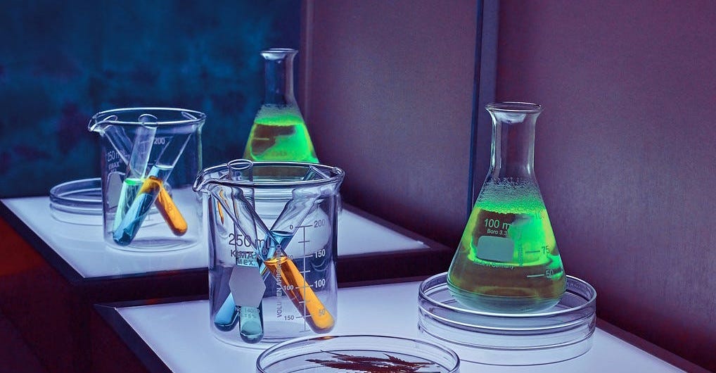 3 test tubes in a beaker next to a large tube of green liquid on a petri dish