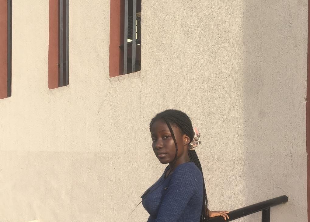 A black lady posing in front of a building with her hand resting on a hand rail