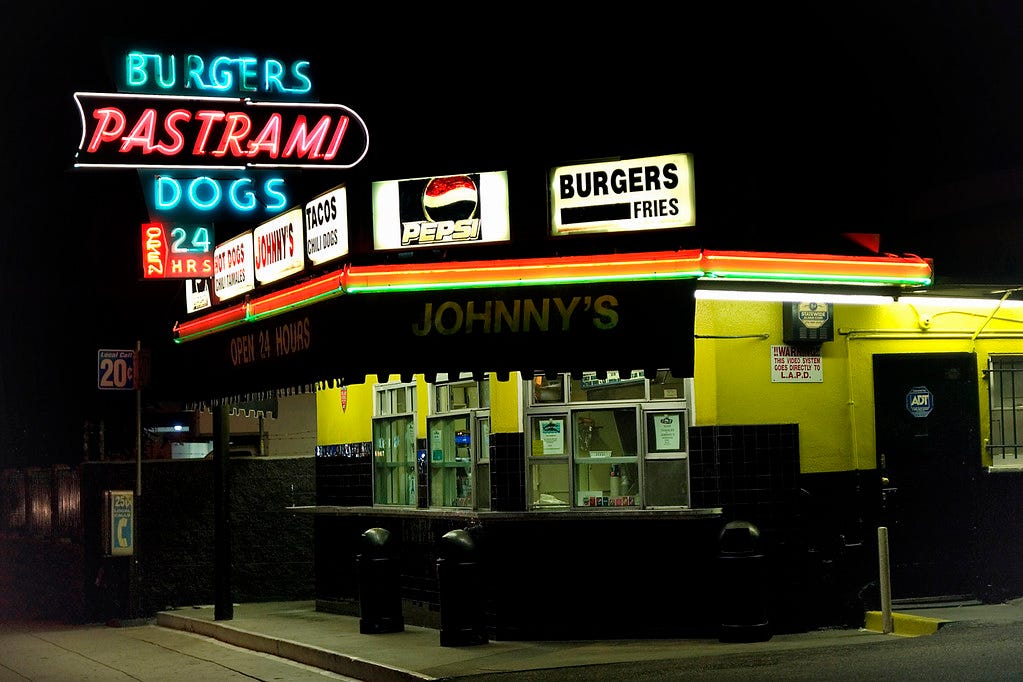 Outside of Johnny’s Pastrami restaurant with blue and pink neon signs