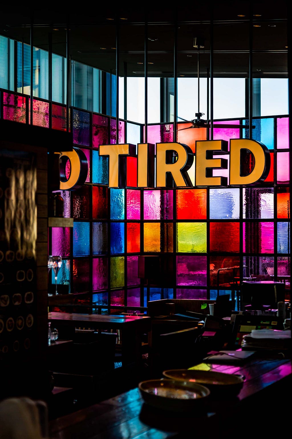 The word ‘tired’ hangs from the ceiling like a light in front of a stained glass window.