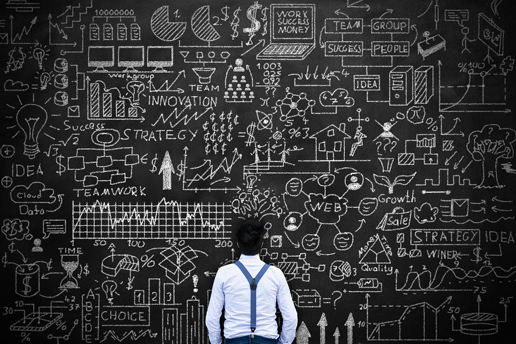 A man standing in front an oversized blackboard with a chaotic overload of information drawn representing a data chaos.