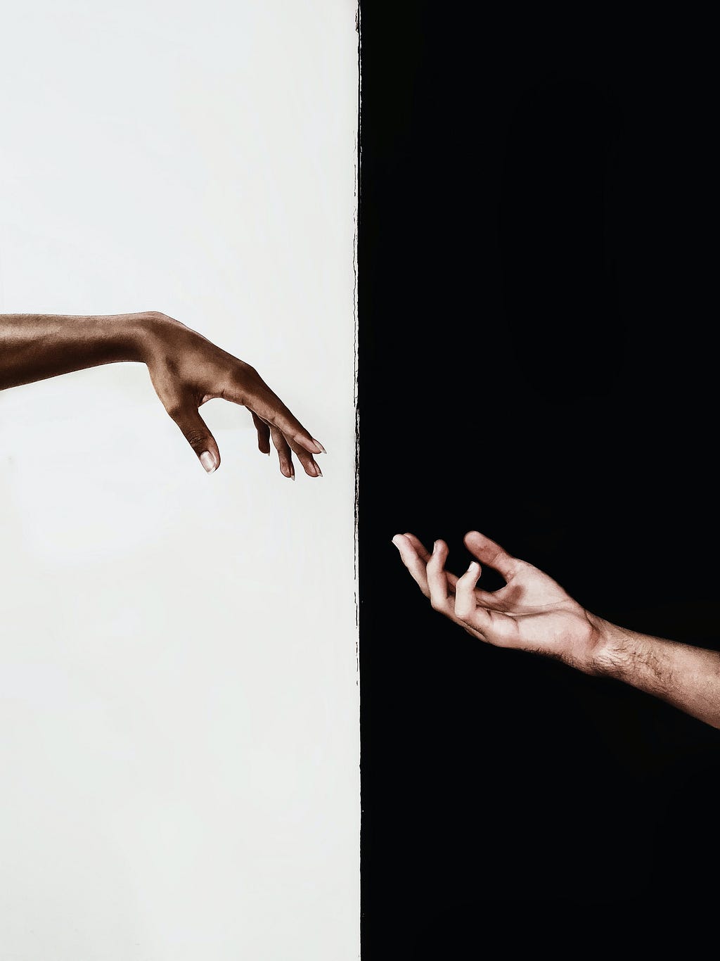 Two arms reaching out to each other. One arm has a white background, while the other has a black background.