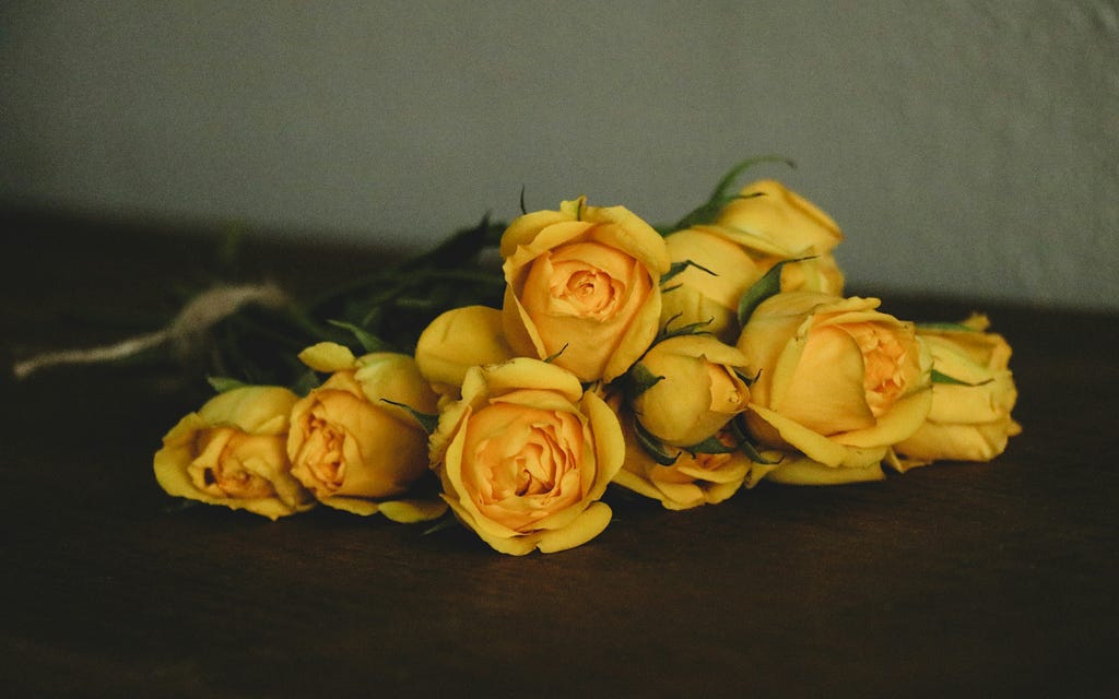 A bundle of yellow roses tied with twine rests on a polished wooden surface.
