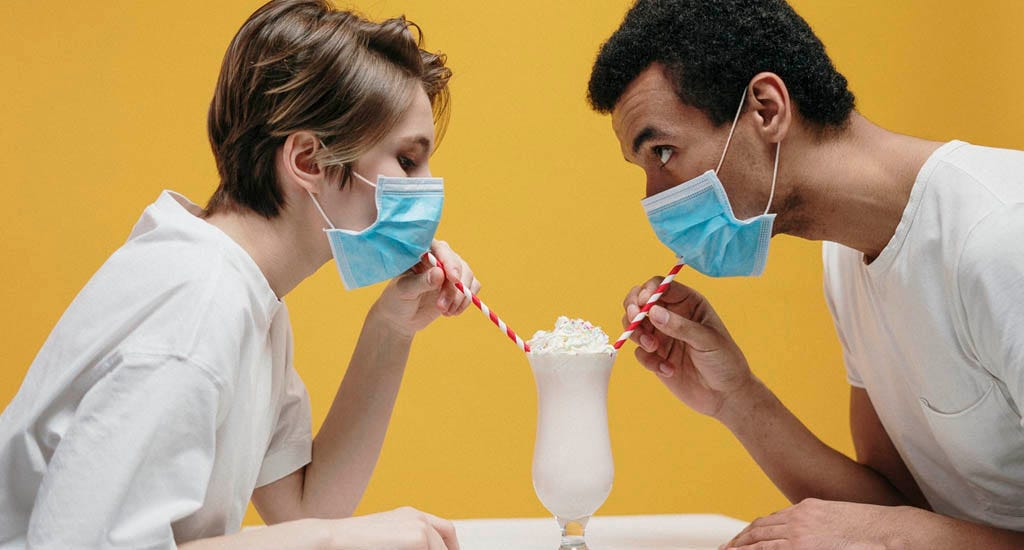Woman and man wearing masks and drinking milkshake through straws on date during COVID-19 pandemic