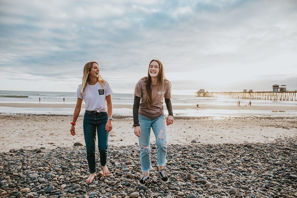 Two friends laughing and chatting on a beach front