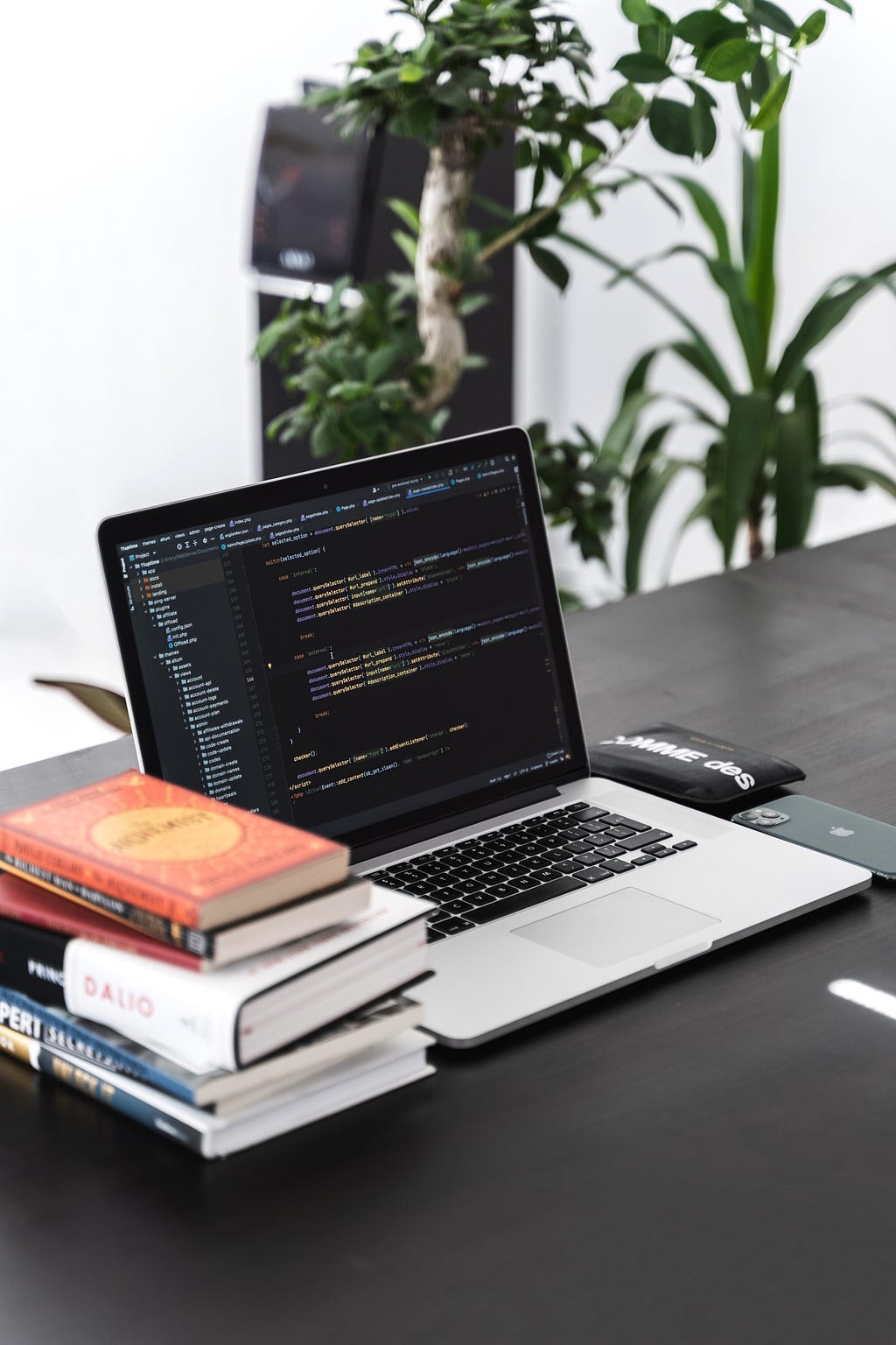 A stack of books and a laptop computer with computer code and a phone.