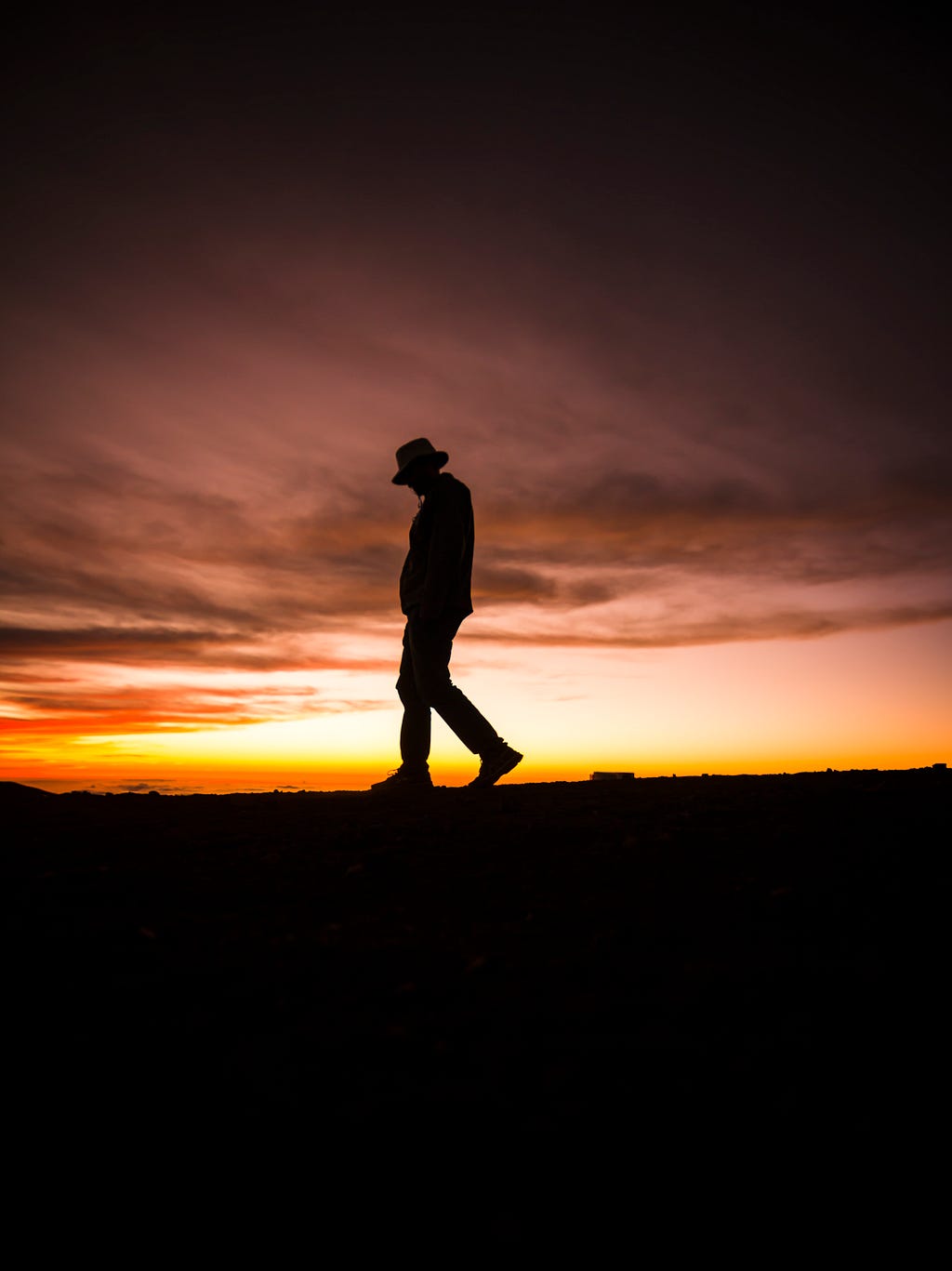 A shadowy figured man walking across an open field during sunset