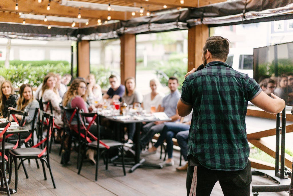 A man with his back to us speaking to a room full of people.