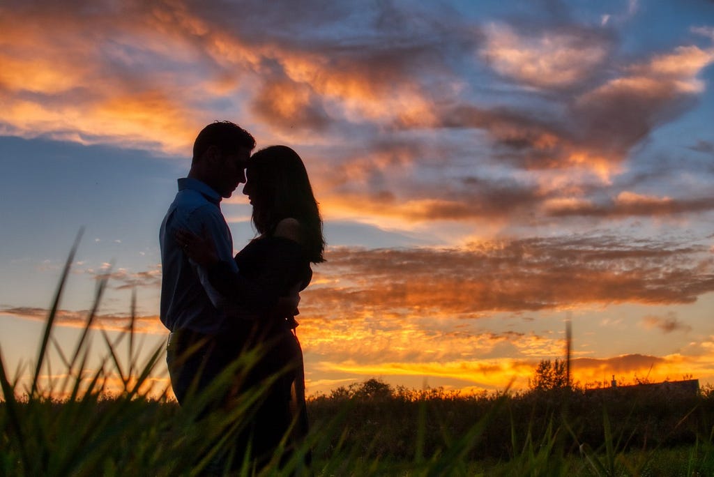 A couple embracing each other endearingly in front of a romantic sunset