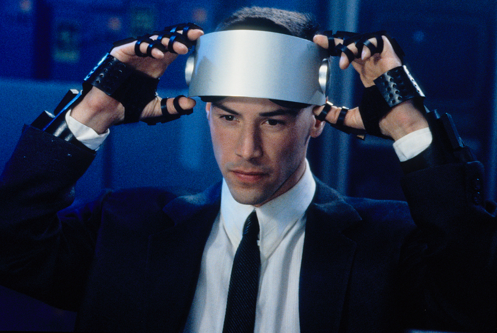 Keanu in Johnny Mneumonic. He is lifting a metal visor above his eyes with both hands, and has a reflective expression.