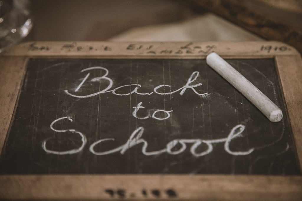 Image of an old-fashioned slate chalkboard with the message “Back to School” written on it in cursive. A piece of chalk is seen resting against the slate chalkboard — alt text to boost Medium stories.