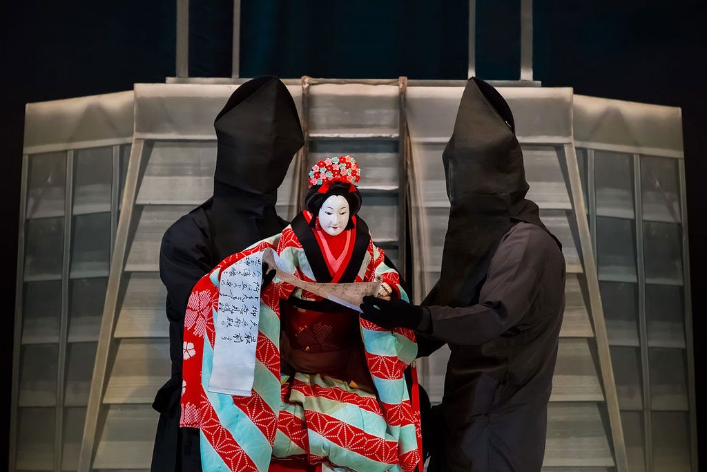 A bunraku performance — two kuroko hold an ornately decorated puppet to enact a traditional story