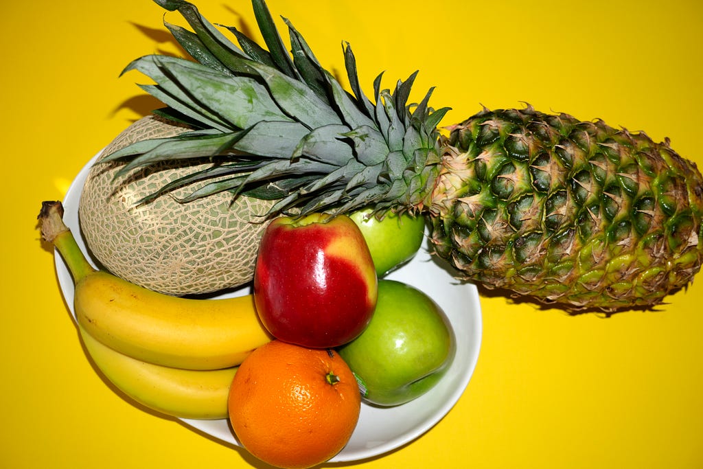 Apples, bananas, pineapple, orange and melon on a yellow background