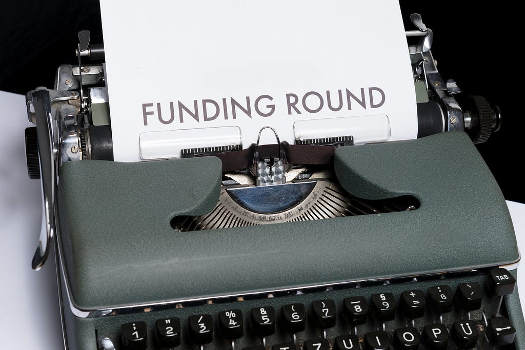 A fax machine displaying a paper half outside with ‘Funding Round’ written on it