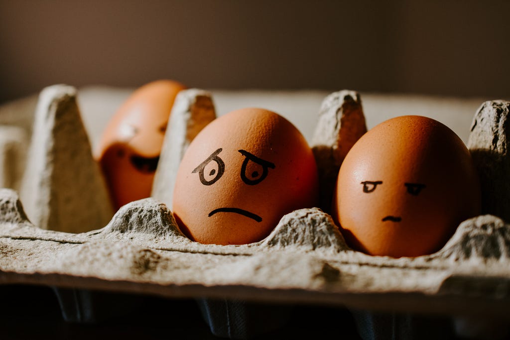 Two visible eggs in a crate, one with a sad, worried face, the other with an upset face