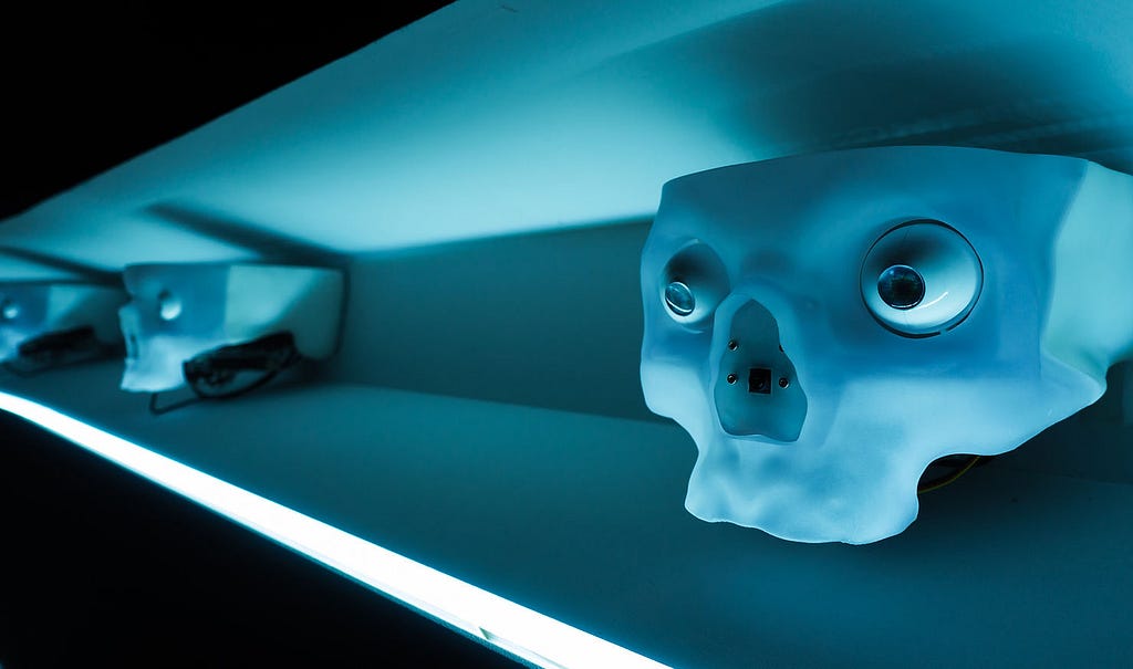 Robot skulls positioned eerily on a dimly lit blue shelf