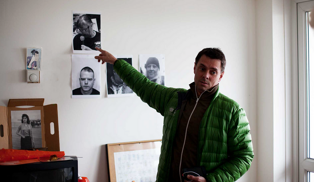 A production image for Operation Black Antler which shows a man in a green coat pointing at mugshots pinned to a wall