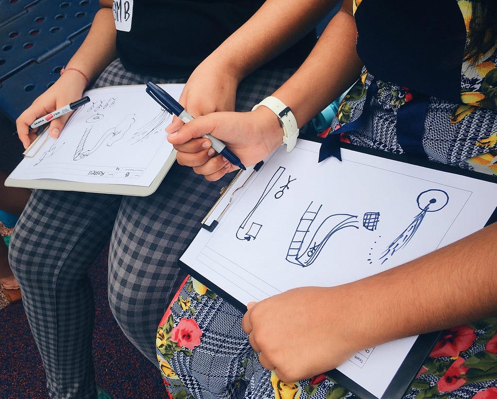 Kids drawing on paper what they wanted their dream playground t look like, with water features