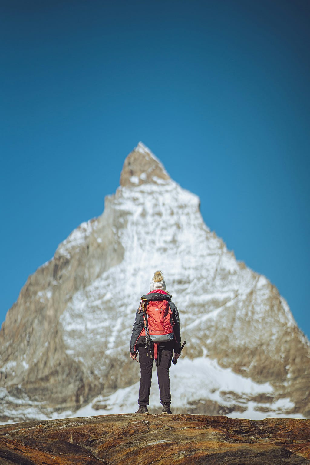 A person climbing a huge mountain with a clear blue sky behind the peak.