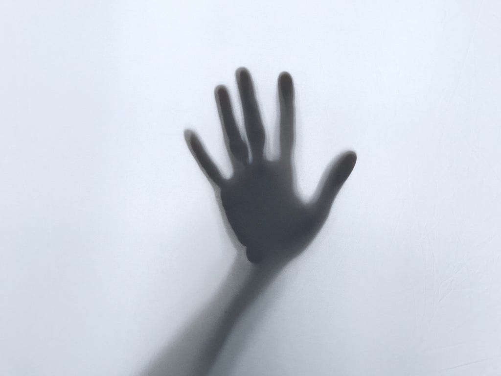 A hand is pressed against a mirror. The rest of the arm is in shadows.