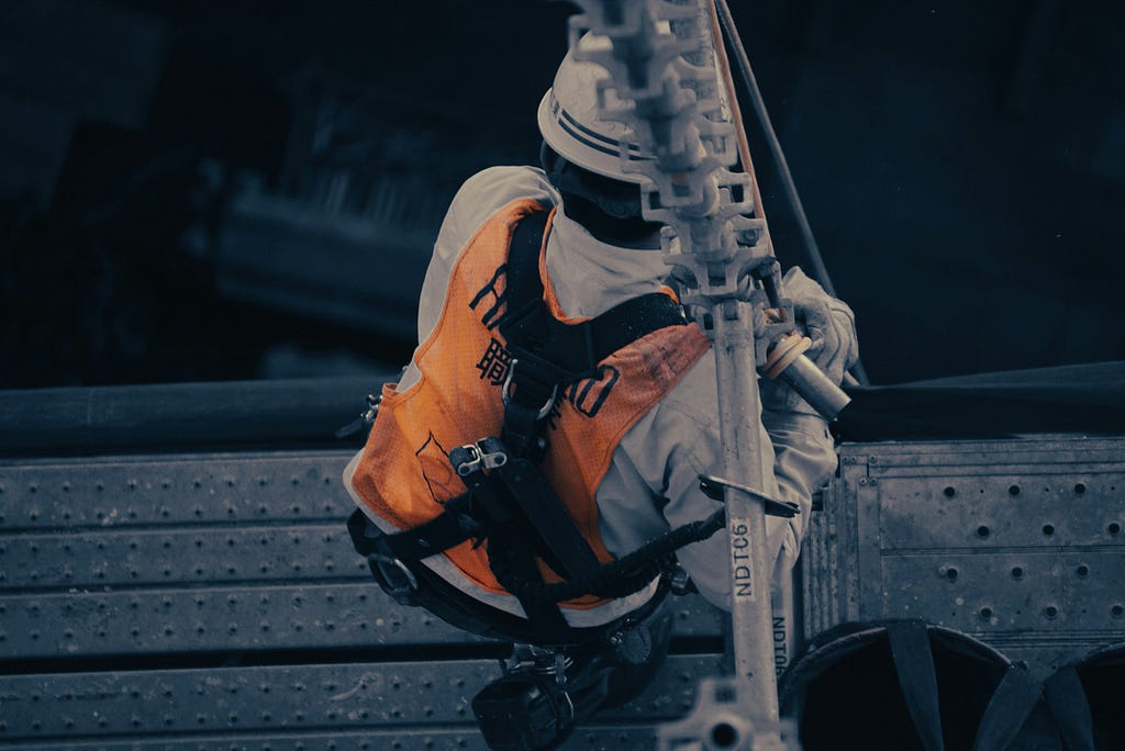 Japanese man wearing white hard hat and orange vest on top of a building