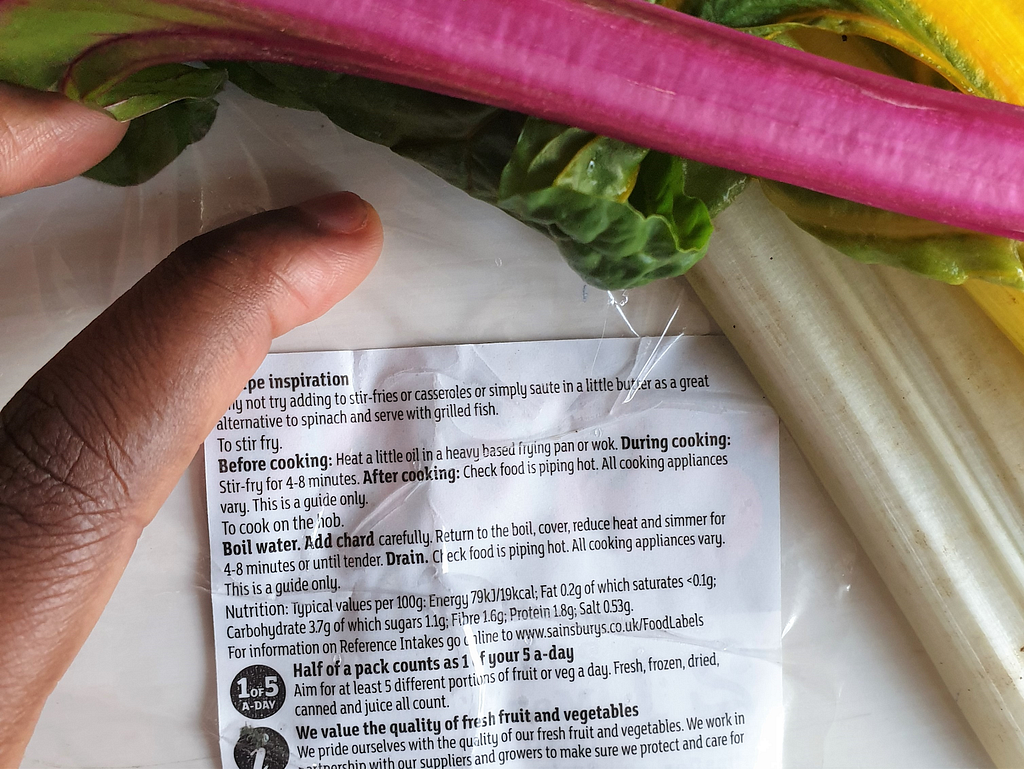 Hand holding food packet with label of nutrition content of rainbow chard and leaves on top