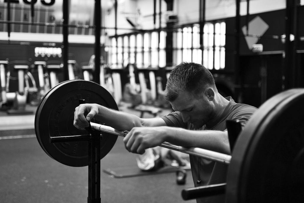 A lifter in leaning on a barbell, looking focused, in black and white.