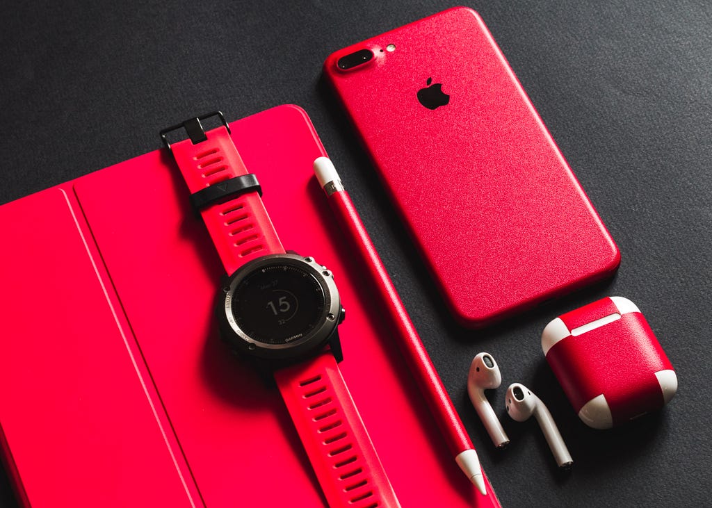 An all red, black and white set of different wearable techs such as Air Pods and a Smart Watch.