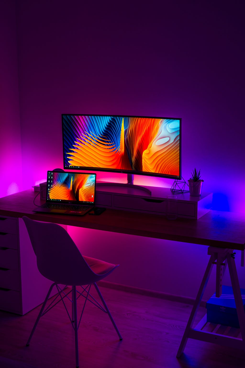 Computer desk with colorful backdrop featuring a color computer screen and laptop screen.